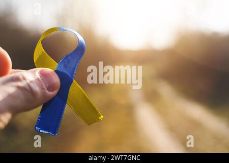 16. März 2024: Hand hält ein gelb-blaues Band in Solidarität mit dem World Down Syndrome Day. FOTOMONTAGE *** Hand hält ein gelb blaues Band zur Solidarität zum Welt Down Syndrom Tag. FOTOMONTAGE Stockfoto