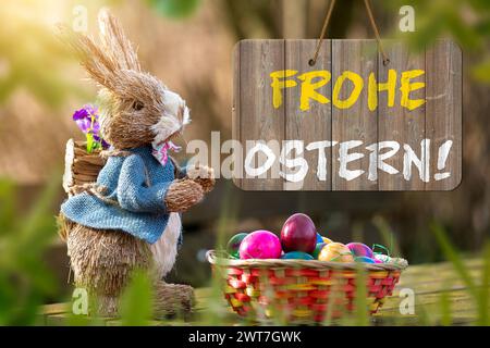 16. März 2024: Frohe Ostergrüße auf einem Schild neben einem Osterhasen mit Osternest und bunten Eiern. FOTOMONTAGE *** Frohe Ostern Grüße zum Osterfest auf einem Schild neben einem Osterhasen mit Osternest und bunten Eiern. FOTOMONTAGE Stockfoto