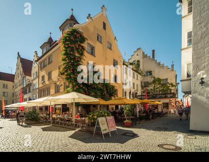 Maximilianstraße in Lindau Altstadt - gelbes Haus an der Ecke einer belebten Straße mit Cafés und Touristen. Sonniger Nachmittag im Mittelalter in der Altstadt. Stockfoto
