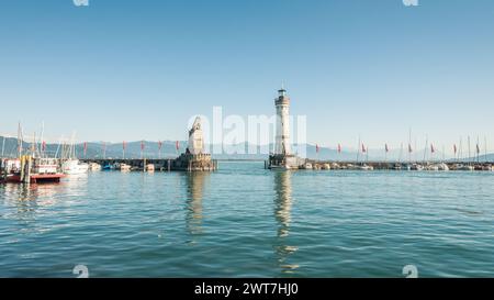 Leuchtturm und Löwenstatue am Eingang zum Hafen von Lindau an einem sonnigen Nachmittag. Ein anderes Ufer des Sees ist im Hintergrund zu sehen. Zahlreiche Boote. Stockfoto