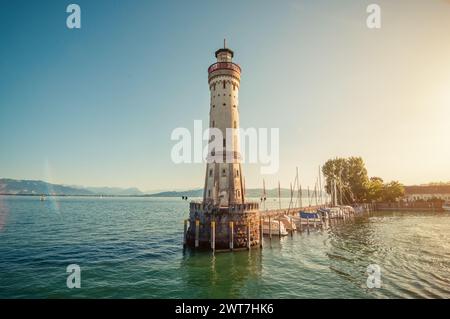 Leuchtturm am Eingang zum Hafen von Lindau an einem sonnigen Nachmittag. Ein anderes Ufer des Sees ist im Hintergrund zu sehen. Segelboote in der Nähe des Piers. Stockfoto