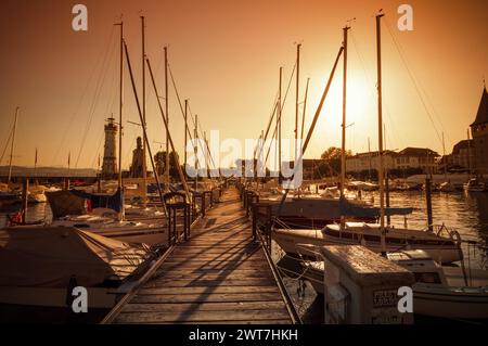 Sonnenuntergang im Hafen von Lindau. Orangefarbenes Bild von zahlreichen verankerten Booten und Segelbooten. Niedrige Sonne und lange Schatten, perspektivische Sicht auf den Bootssteg. Stockfoto