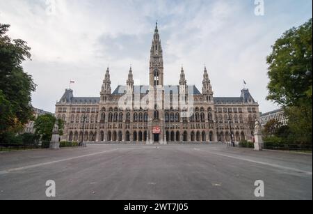 Symmetrische Ansicht des Wiener Rathauses. Neogotisches Rathaus und leerer Platz davor, grüne Bäume an den Seiten. Bewölkter Tag. Stockfoto