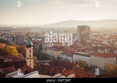 Blick aus der Vogelperspektive von Graz bei Sonnenuntergang. Stadtübersicht vom Schlossberg mit Franziskanerkirche in der Mitte und Ziegeldächern von Gebäuden in der Nähe. Stockfoto