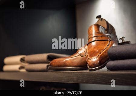 Regal mit braunen, handgefertigten Schuhen und ein paar gefalteten Pullover. Kleiderschrank mit Männerkostümen. Kleiderschrank in Bekleidungsboutique. Dunkelbraune Möbel. Stockfoto