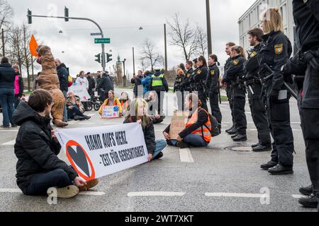 Regensburg, Deutschland. März 2024. Demonstranten, die auf der Straße sitzen, blockieren die Kreuzung Kumpfmühler Str. und Fritz-Fend-Straße. Polizeibeamte stehen in unmittelbarer Nähe. Die letzte Generation protestiert gegen die Klimapolitik der Ampelregierung. Quelle: Daniel Vogl/dpa/Alamy Live News Stockfoto