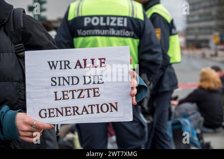 Regensburg, Deutschland. März 2024. Auf dem Schild eines Demonstrators steht: „Wir sind alle die letzte Generation“. Polizeibeamte stehen im Hintergrund und Demonstranten sitzen auf dem Boden. Die letzte Generation protestiert gegen die Klimapolitik der Ampelregierung. Quelle: Daniel Vogl/dpa/Alamy Live News Stockfoto