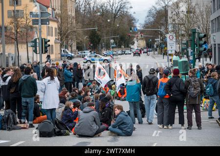 Regensburg, Deutschland. März 2024. Demonstranten stehen und sitzen auf der Straßenblockade die Kreuzung Kumpfmühler Str. und Fritz-Fend-Straße. Die letzte Generation protestiert gegen die Klimapolitik der Ampelregierung. Quelle: Daniel Vogl/dpa/Alamy Live News Stockfoto