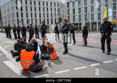 Regensburg, Deutschland. März 2024. Demonstranten, die auf dem Boden sitzen, blockieren die Kreuzung von Kumpfmühler Str. und Fritz-Fend-Str. In der Nähe des Bahnhofs. Polizeibeamte stehen in unmittelbarer Nähe. Die letzte Generation protestiert gegen die Klimapolitik der Ampelregierung. Quelle: Daniel Vogl/dpa/Alamy Live News Stockfoto