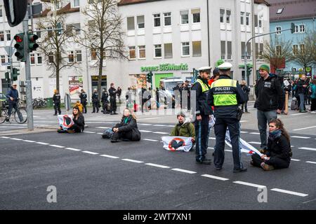 Regensburg, Deutschland. März 2024. Demonstranten stehen und sitzen auf der Straßenblockade die Kreuzung Kumpfmühler Str. und Fritz-Fend-Straße. Die letzte Generation protestiert gegen die Klimapolitik der Ampelregierung. Quelle: Daniel Vogl/dpa/Alamy Live News Stockfoto