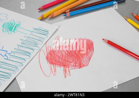 Niedliche Kinderzeichnungen und bunte Bleistifte auf grauem Tisch Stockfoto