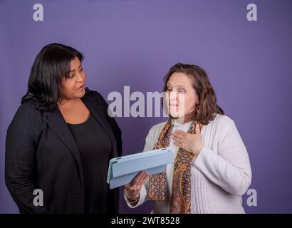 Zwei Frauen reden miteinander, eine von ihnen hält eine Tafel. Die Tablette ist blau und die Frau trägt eine schwarze Jacke. Die Szene ist lässig und Stockfoto