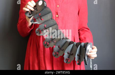 Halloween-Vorbereitungen. Junge Frau mit festlicher Girlande auf schwarzem Hintergrund mit Kopierraum. Halloween-Dekorationen aus nächster Nähe Foto. Stockfoto