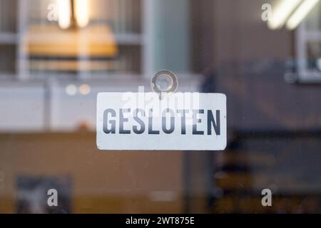 Weiß ein rotes Schild, das an der Glastür eines Ladens hängt und auf Niederländisch steht: 'Gesloten', was im Englischen 'geschlossen' bedeutet. Stockfoto