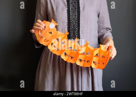 Halloween-Vorbereitungen. Junge Frau mit festlicher Girlande auf schwarzem Hintergrund mit Kopierraum. Halloween-Dekorationen aus nächster Nähe Foto. Stockfoto