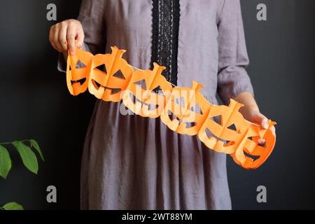 Halloween-Vorbereitungen. Junge Frau mit festlicher Girlande auf schwarzem Hintergrund mit Kopierraum. Halloween-Dekorationen aus nächster Nähe Foto. Stockfoto