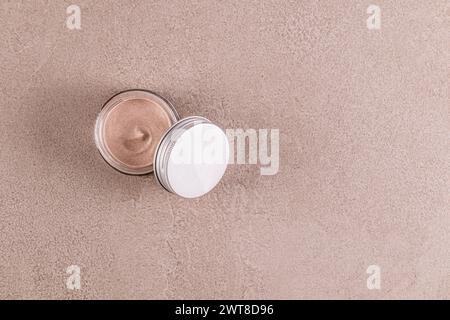 Offenes Glasgefäß mit silbernem Deckel mit Körpercreme, Peeling Peeling auf beigefarbenem Steinhintergrund. Draufsicht. Ein Kopierbereich. Schönheitskonzept. Spa Stockfoto