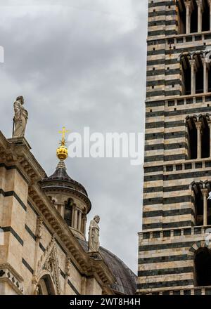 Architektonische Details der Kathedrale von Siena (Dom) mit ihren berühmten weißen und schwarzen Marmorstreifen des Glockenturms, Skulpturen und einem goldenen Kreuz darüber Stockfoto