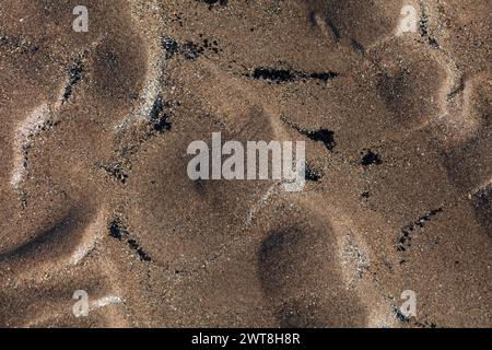 Die rückläufige Flut hinterließ im Sand ein sich wiederholendes Muster aus kleinen Unebenheiten mit Wasserkanälen und kleinen Mengen Schwarzkohlestaub, um das Relief zu verstärken Stockfoto