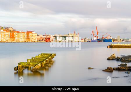 Ein ruhiger Morgen im Hafen von Göteborg in Schweden, wenn die Sonne aufgeht und ein moosbedecktes hölzernes Dock hervorhebt, das sich in das ruhige Wasser hineinzieht. Das b Stockfoto