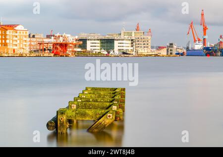 Ein ruhiger Morgen im Hafen von Göteborg in Schweden, wenn die Sonne aufgeht und ein moosbedecktes hölzernes Dock hervorhebt, das sich in das ruhige Wasser hineinzieht. Das b Stockfoto