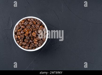 Weiße Keramikschale mit gerösteten Kaffeebohnen auf einem leeren dunklen Hintergrund, Draufsicht. Kopierbereich Stockfoto