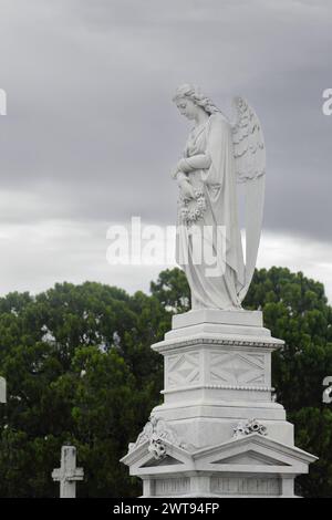 Weibliche Engelsstatue auf einem Sockel, beide aus weißem Marmor, auf dem Cementerio de Colon Friedhof, der für seine vielen kunstvoll gestalteten Gedenkstätten bekannt ist, estima Stockfoto