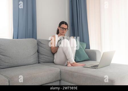 Eine Frau, die auf einer Couch sitzt, denkt und schreibt Notizen. Stockfoto