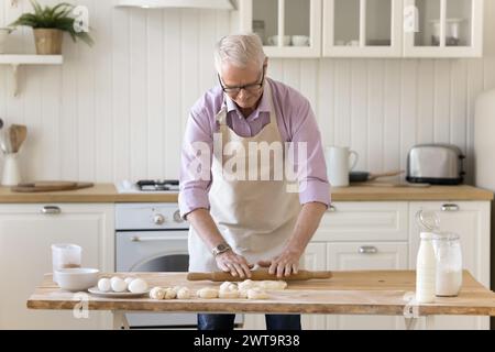 Fokussierter älterer Mann, der Teig für Brötchen platt Stockfoto