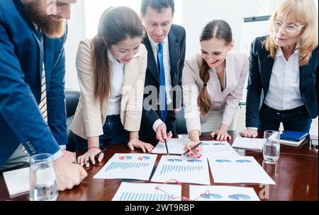 Multiethnisches Team von engagierten Spezialisten, die verschiedene Diagramme über Gewinn und Entwicklung des Unternehmens analysieren Stockfoto