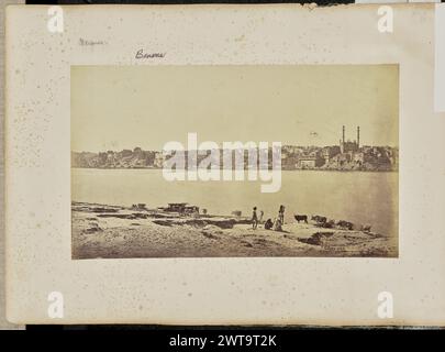 Benares; allgemeine Ansicht vom gegenüberliegenden Ganges. Samuel Bourne, Fotograf (Deutsch, 1834 – 1912) 1865–1866 Blick auf eine Stadt am Flussufer, vom gegenüberliegenden Ufer des Flusses aus gesehen. Im mittleren rechten Bildbereich ist eine Moschee zu sehen, die von drei großen Kuppeln und zwei hoch aufragenden Minaretten gekrönt ist. Entlang des Ufers kann man eine Reihe von Ghats oder Flussstufen sehen, die normalerweise für religiöse Zwecke genutzt werden. Im Vordergrund sind vier Ureinwohner mit einer Rinderherde zu sehen. (Recto, bedruckt) unten rechts, mit der Negativbeschriftung: '1165'; (Recto, Mount) oben links, mit Bleistift: ' Stockfoto