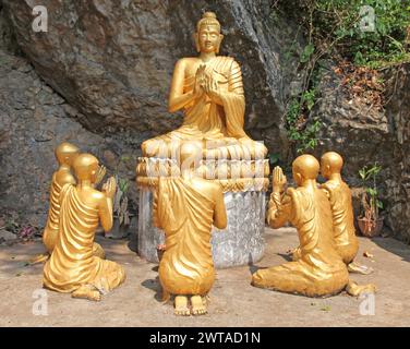 Buddha-Statue mit Mönchen, die beten. Der Buddhismus ist ein integraler Bestandteil des Lebens in Luang Prabang, der zum UNESCO-Weltkulturerbe gehört Stockfoto