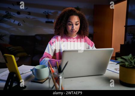 Junge müde afroamerikanische Universitätsfrau, die am Schreibtisch im Wohnzimmer sitzt. Stockfoto