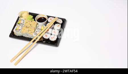 Sushi zum Mitnehmen in einer schwarzen Kiste mit Holzstäbchen auf weißem Hintergrund Stockfoto