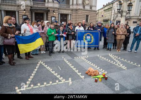 Menschen mit Kerzen in der Hand stehen während der Gedenkveranstaltung neben der Aufschrift „KINDER“. Die Bewohner von Lwiw und die zwangsvertriebenen Bewohner des besetzten Mariupol nehmen an einer Veranstaltung zum Gedenken an die vor 2 Jahren verstorbenen Menschen im Mariupol-Theater in der Nähe des Nationalen Akademischen Operntheaters und Balletts von Solomiya Krushelnytska Teil. Die Bewohner von Mariupol versammelten sich in der Nähe der Theater von Lemberg und vieler Städte der Ukraine und zündeten Gedenklampen an, um an die Toten zu erinnern. Am 16. März 2022 warfen die russischen Besatzungsmitglieder Luftangriffe auf die Theater in Mariupol ab, ohne die zu ignorieren Stockfoto