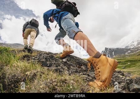 Zwei junge Wanderer mit Rucksäcken spazieren in den Bergen. Nahaufnahme von touristischen Beinen, die bergauf gehen Stockfoto