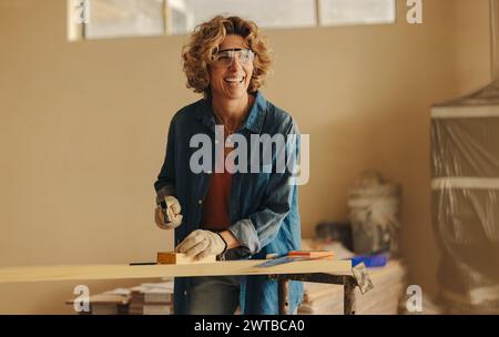 Glückliche weiße Frau baut ihr Haus um und arbeitet an Sockelleisten in der Küche. Sie nagelt geschickt eine Holzplatte mit einem Hammer, Handwerkzeugen und Tresor Stockfoto