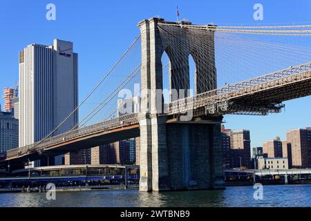 Die Brooklyn Bridge über den Fluss mit Blick auf die Stadt im Hintergrund unter einem klaren blauen Himmel, am East River, Manhattan, Brooklyn, New York City Stockfoto