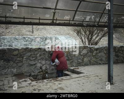 Eine Frau füllt Trinkwasser in einem öffentlichen Brunnen. In den nördlichen und östlichen Stadtvierteln von Charkow wurden viele Wohngebäude zerstört Stockfoto