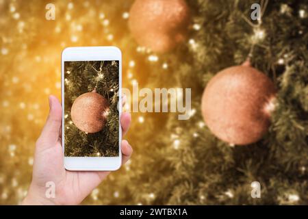 Frau Hand hält Handy-Smartphone, das Bilder von weihnachtsdekorationen auf den Zweigen des Tannenbaums über dem Hintergrund des weihnachtsbaums macht Stockfoto