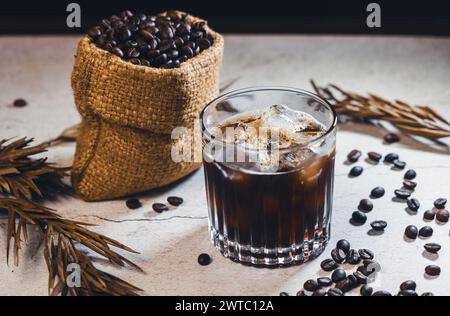 Eiskaffee schwarz im Glas und Kaffeebohnen. Kaltes Sommergetränk auf Holztisch mit Kopierraum. Eiskaffee Americano. Stockfoto