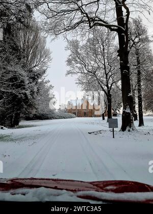 Ein leeres Gebäude steht an Winterbäumen auf einer verschneiten Straße Stockfoto