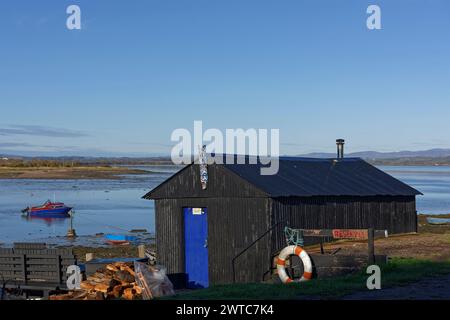 Eine kleine Black Painted Hut aus gewellten Blechplatten mit einem Holzofen, der das Dach verlässt, am Montrose Basin. Stockfoto