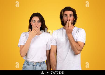 Mann und Frau mit überraschtem Ausdruck, beide bedecken ihren Mund mit den Händen Stockfoto