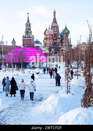 Moskau, Russland - 8. Februar 2024: Menschen auf verschneiten Wegen im öffentlichen Park der Stadt Sarjadje und Blick auf die Basilius-Kathedrale und die Kreml-Türme in Moskau Stockfoto
