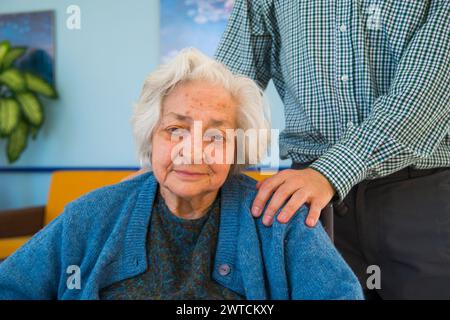 Porträt einer alten Frau in einem Pflegeheim und eines Mannes, der seine Hand auf ihre Schulter legt. Stockfoto
