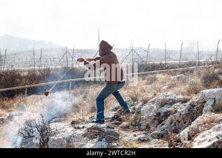 Bilin, Ramallah, Palästina. November 2010. Ein palästinensischer Aktivist wirft einen Stein bei wöchentlichen Freitagsprojekten gegen die Besetzung palästinensischer Gebiete durch Israel in Bilin, Westjordanland, Palästina am 11. November 2010. Bilin, ein kleines Dorf in der Nähe von Ramallah, findet wöchentlich Proteste statt, da ein Großteil des Landes der Bauern von den israelischen Behörden annektiert wurde, um eine neue jüdische Siedlung zu bauen. (Credit Image: © Dominika Zarzycka/SOPA images via ZUMA Press Wire) NUR REDAKTIONELLE VERWENDUNG! Nicht für kommerzielle ZWECKE! Stockfoto