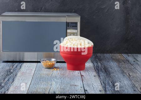 Popcorn in der Schüssel in der Nähe der Mikrowelle auf dem Tisch in der Küche auf schwarzem Hintergrund Stockfoto