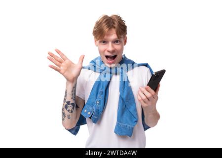 Der junge charmante, schlanke rothaarige Mann mit einem kurzen Haarschnitt und einem Tattoo auf den Armen trägt ein stilvolles blaues Hemd Stockfoto