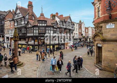 Shopper, die über nasse Gehwege und Kopfsteinpflaster in der römischen Stadt Chester England spazieren, um das mittelalterliche Kreuz und die Geschäfte in den Reihen Stockfoto